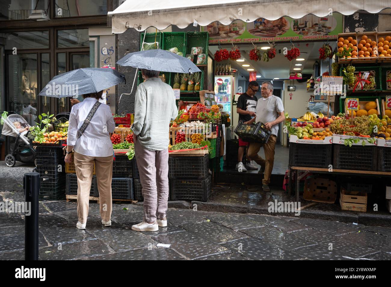 Touristen mit Sonnenschirmen schauen auf einen Obst- und Gemüsemarkt in Neapel Stockfoto