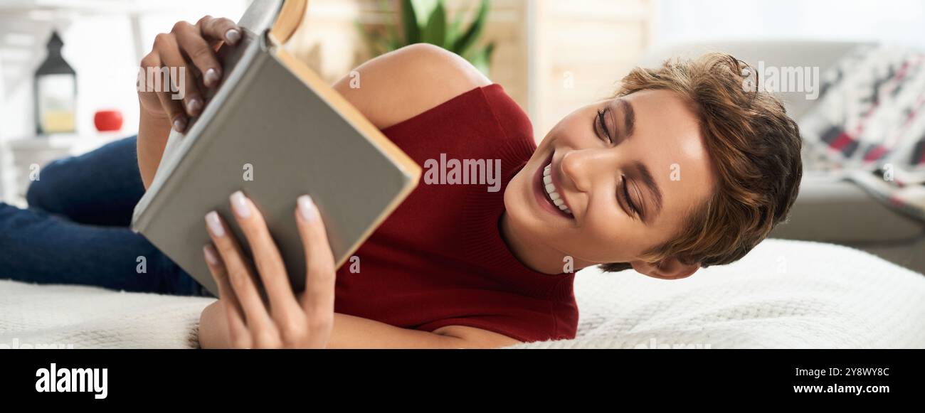 Eine junge Frau mit kurzen Haaren entspannt sich zu Hause, tief in ihr Buch vertieft, während sie lässig angezogen ist. Stockfoto