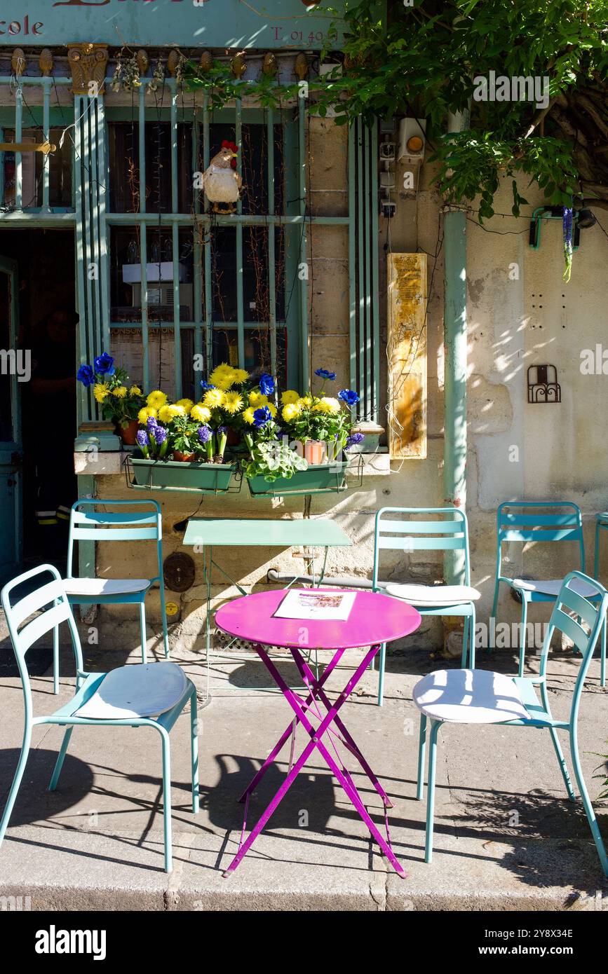 Pinkfarbener Tisch und pastellgrüne Stühle vor dem ältesten Restaurant in Paris. Schöne leuchtend gelbe, blaue und lila Blumen. Blauer Mohn, Hyazinthe Stockfoto