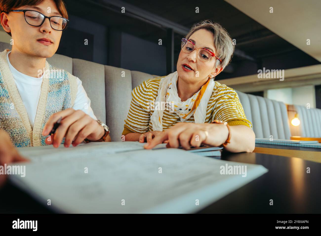 Ein Schüler und Tutor, der in einem College-Setting zusammenarbeitet, sich auf Lehrmaterialien konzentriert und sich an einer durchdachten Diskussion beteiligt. Die Umwelt ist Stockfoto