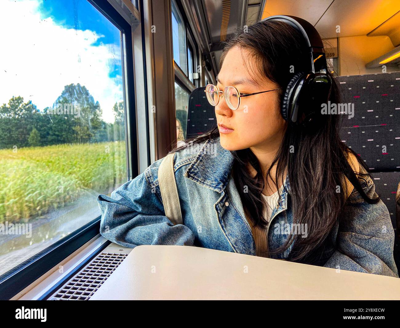 Junge Erwachsene, weibliche Pendlerinnen, die mit dem Zug durch Westflandern reisen und gleichzeitig nach draußen schauen, um die belgische Landschaft zu betrachten. Stockfoto