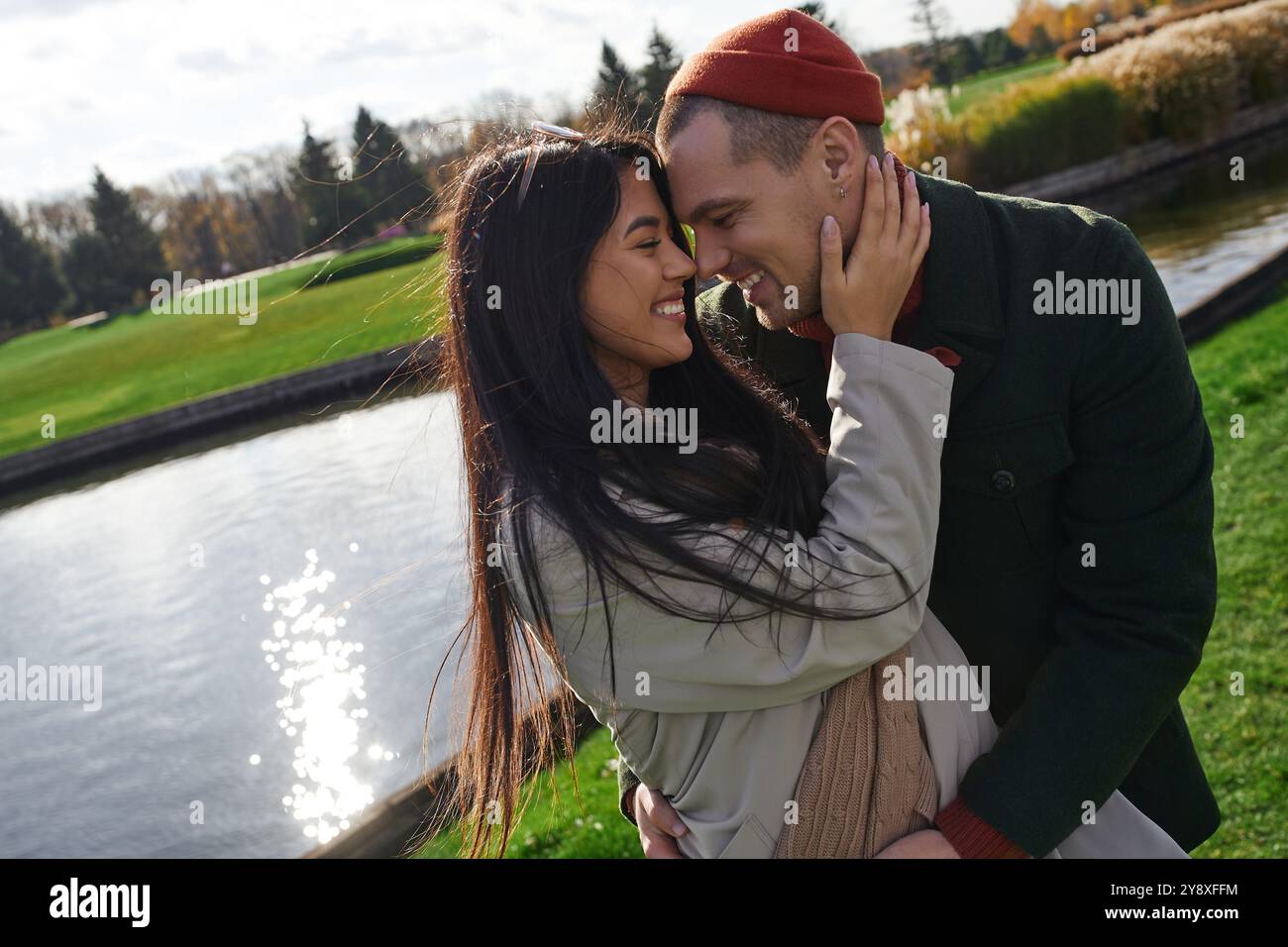 Ein Paar teilt sich eine warme Umarmung am Wasser und sonnt sich mit einem Lächeln in der hellen Herbstsonne. Stockfoto