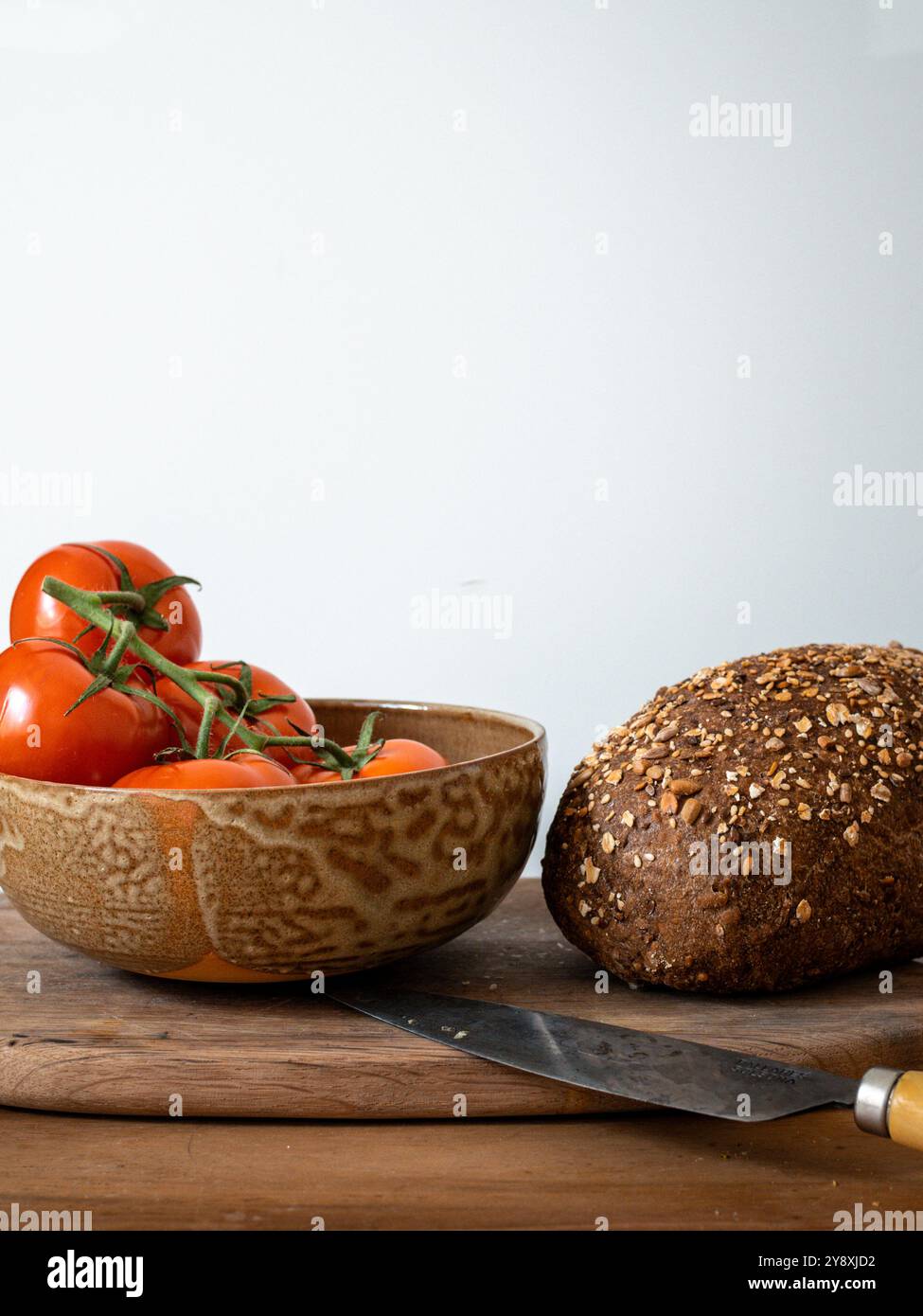 Frische Tomaten, Vollkornbrot auf einem rustikalen Holzbrett mit glänzendem Messer Stockfoto