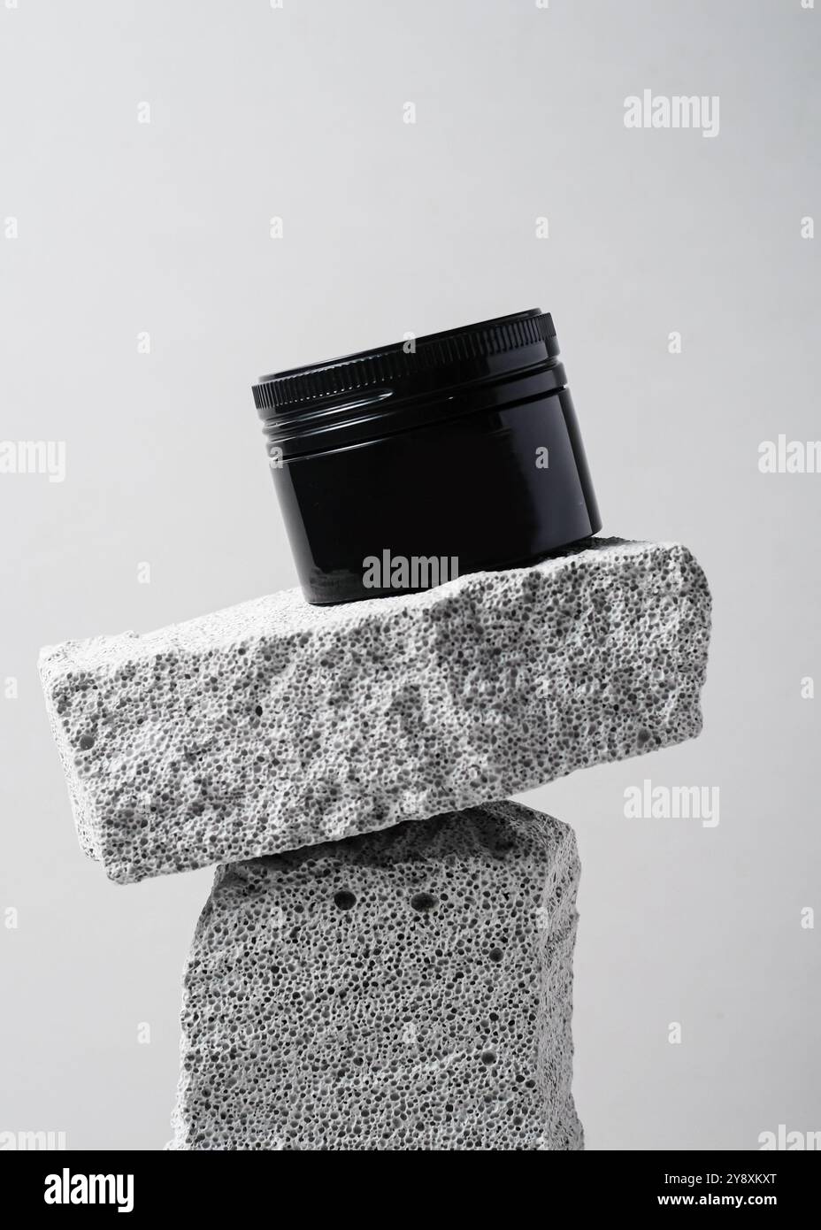 Ein elegantes schwarzes Kosmetikglas mit minimalistischem Design vor einem strukturierten weißen Steinhintergrund. Dieses klare und elegante Image ist perfekt für Showca Stockfoto