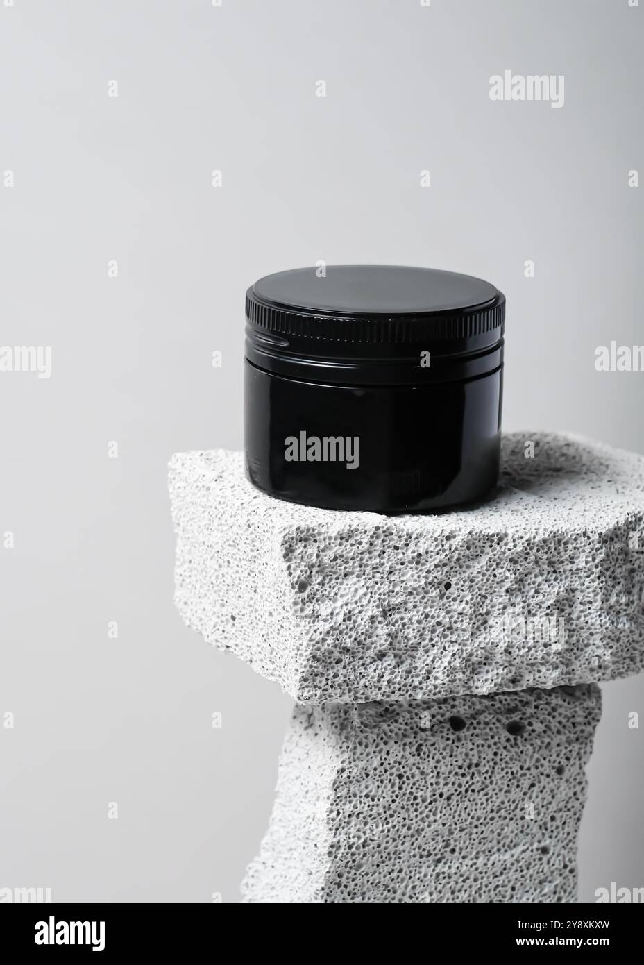 Ein elegantes schwarzes Kosmetikglas mit minimalistischem Design vor einem strukturierten weißen Steinhintergrund. Dieses klare und elegante Image ist perfekt für Showca Stockfoto