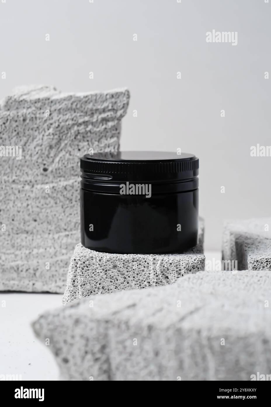 Ein elegantes schwarzes Kosmetikglas mit minimalistischem Design vor einem strukturierten weißen Steinhintergrund. Dieses klare und elegante Image ist perfekt für Showca Stockfoto