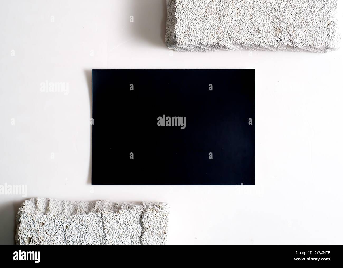 Ein raffiniertes Modell mit schwarzer Karte, das elegant vor einem sauberen weißen Steinhintergrund dargestellt wird. Dieses minimalistische Design unterstreicht das schlanke Design Stockfoto