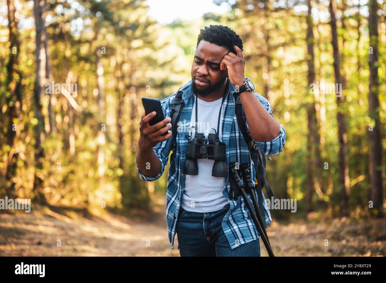 Ein besorgter Wanderer hat sich verirrt und er benutzt ein Telefon, um die richtige Richtung zu finden, während er in der Natur wandert. Stockfoto