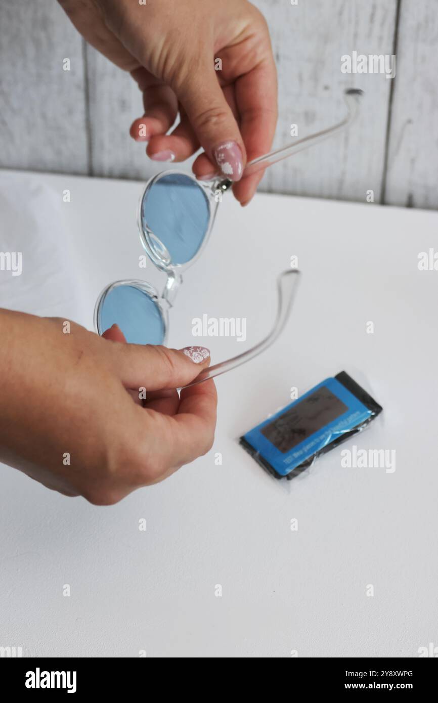 Eine Frau überprüft die Polarisation einer Sonnenbrille mit blauen Gläsern. Sie prüft einen Kauf auf einer Marketplace-Site. Stockfoto