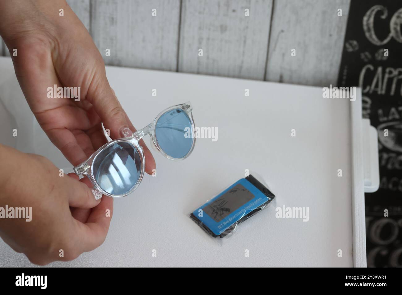 Eine Frau überprüft die Polarisation einer Sonnenbrille mit blauen Gläsern. Sie prüft einen Kauf auf einer Marketplace-Site. Stockfoto