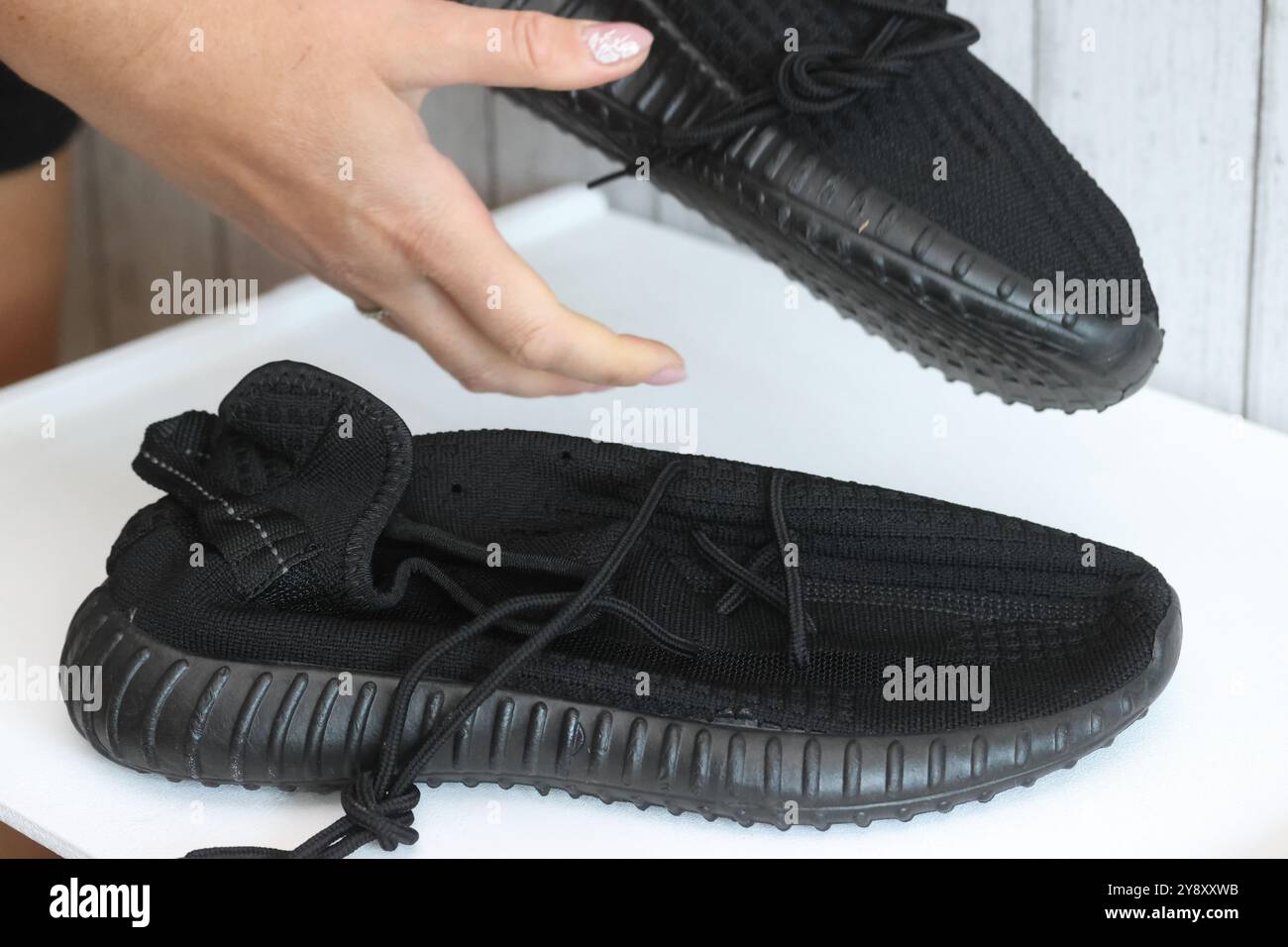 Eine Frau überprüft schwarze Sneakers. Demonstration eines auf einer Marketplace-Site getätigten Kaufs. Stockfoto