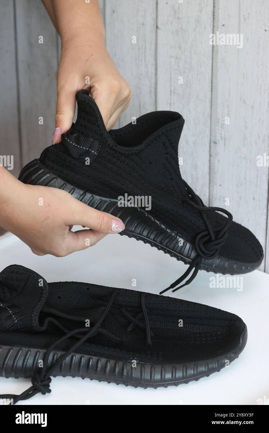 Eine Frau überprüft schwarze Sneakers. Demonstration eines auf einer Marketplace-Site getätigten Kaufs. Stockfoto