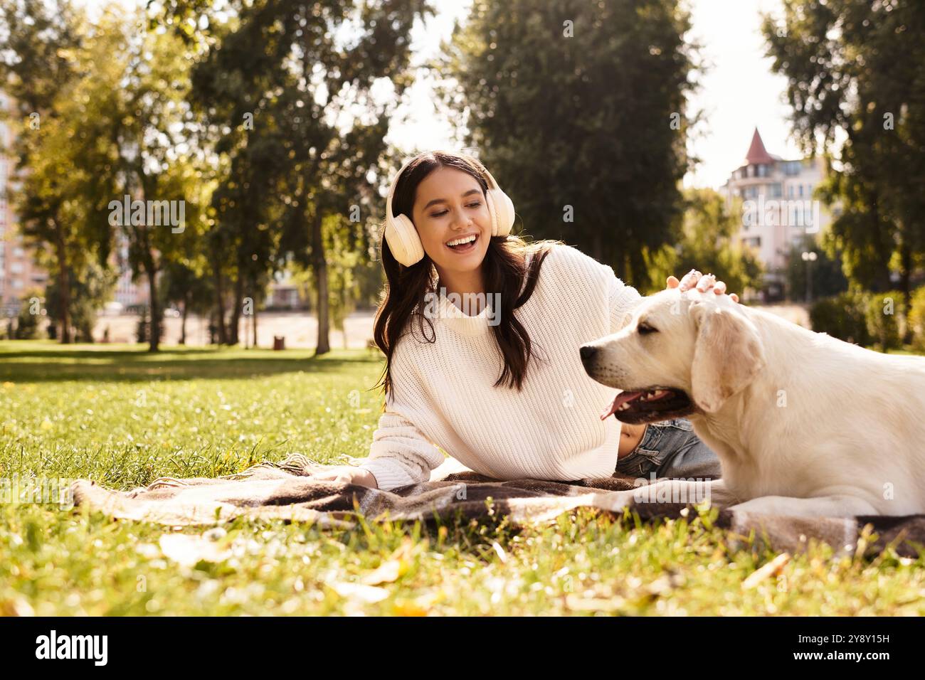 Eine fröhliche junge Frau entspannt sich auf dem Gras und interagiert glücklich mit ihrem Hund in einem lebhaften Park. Stockfoto