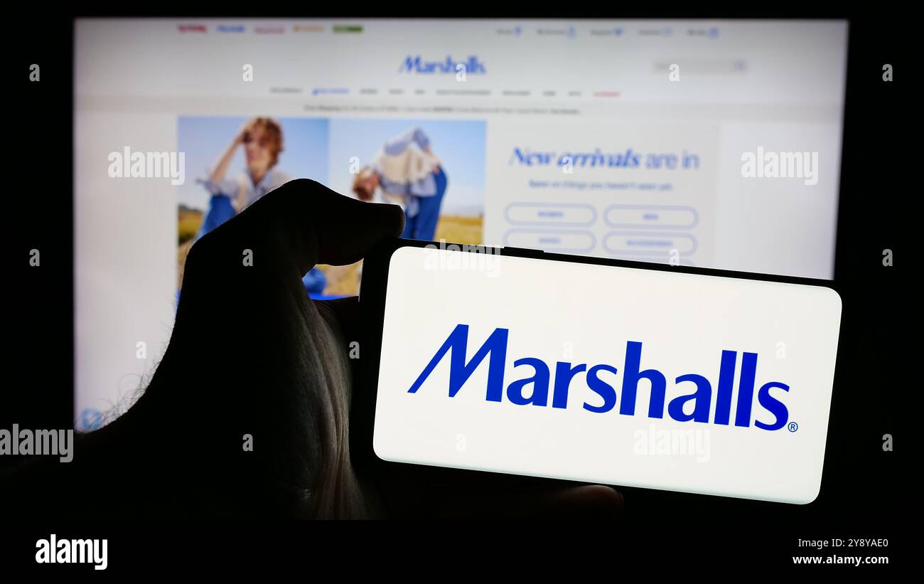 Person, die ein Mobiltelefon mit dem Logo der amerikanischen Kaufhausfirma Marshalls Inc. Auf dem Bildschirm vor der Webseite hält. Schwerpunkt auf dem Display des Telefons. Stockfoto