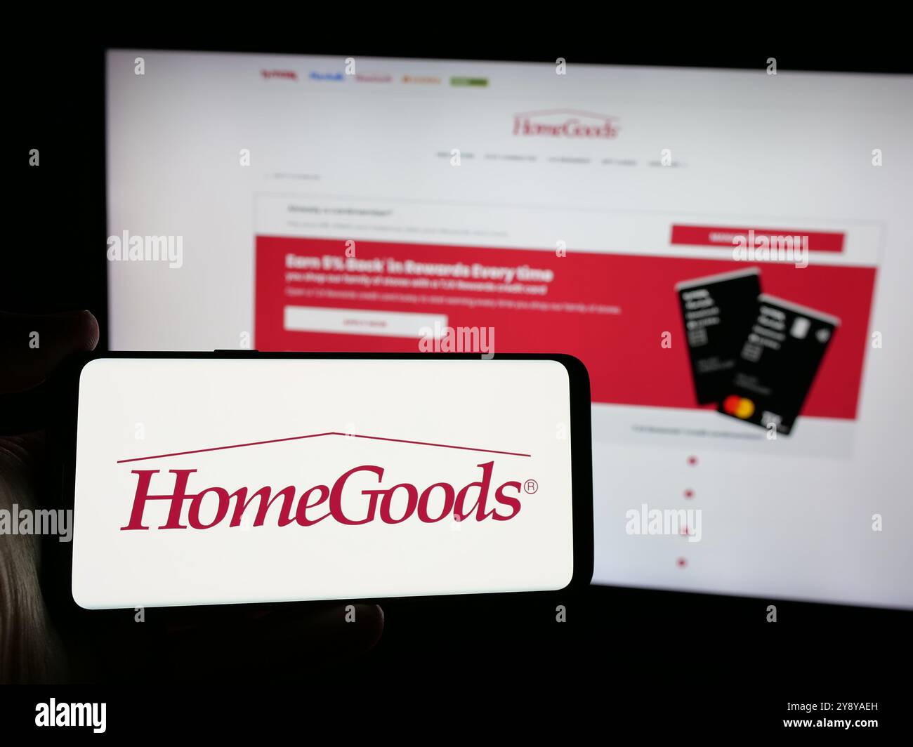 Person, die ein Smartphone mit dem Logo des US-amerikanischen Einrichtungsunternehmens HomeGoods auf dem Bildschirm vor der Website hält. Schwerpunkt auf dem Display des Telefons. Stockfoto