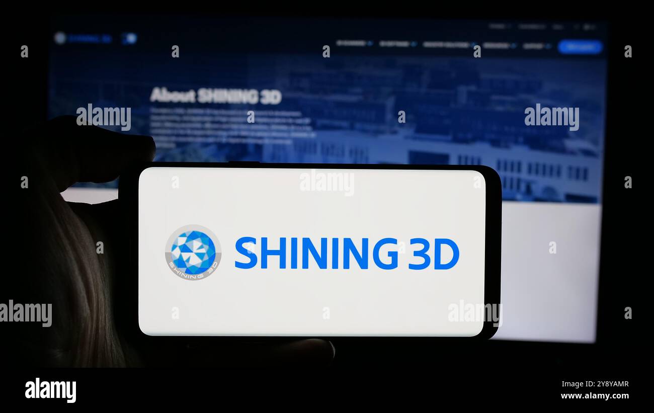 Person, die ein Mobiltelefon mit dem Logo des chinesischen Unternehmens Hangzhou Shining 3D Co. Ltd. Auf dem Bildschirm vor der Webseite hält. Schwerpunkt auf dem Display des Telefons. Stockfoto