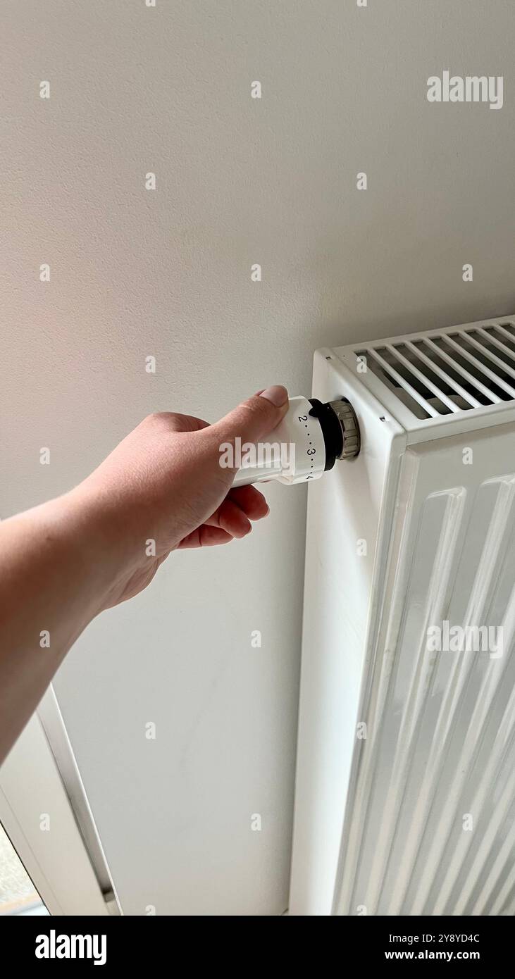 Die Hand einer Frau regelt die Temperatur auf dem Heizkörper. Nahaufnahme des Heizkörpers in der Wohnung. Der Beginn der Heizsaison, Erwärmung von t - Smartphone-aufgenommenes Stockfoto