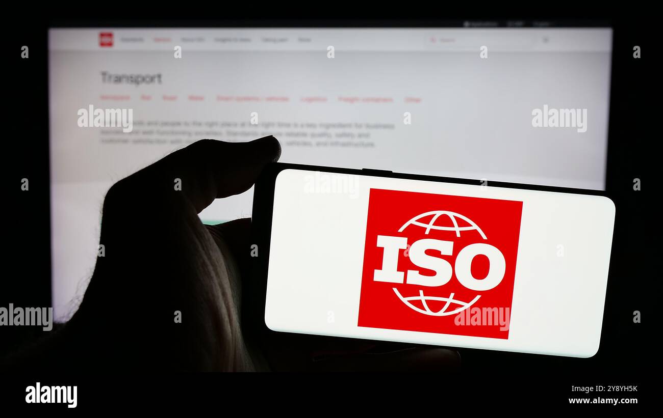 Person, die ein Mobiltelefon mit dem Logo der Internationalen Organisation für Normung (ISO) auf dem Bildschirm und der Website hält. Schwerpunkt auf dem Display des Telefons. Stockfoto