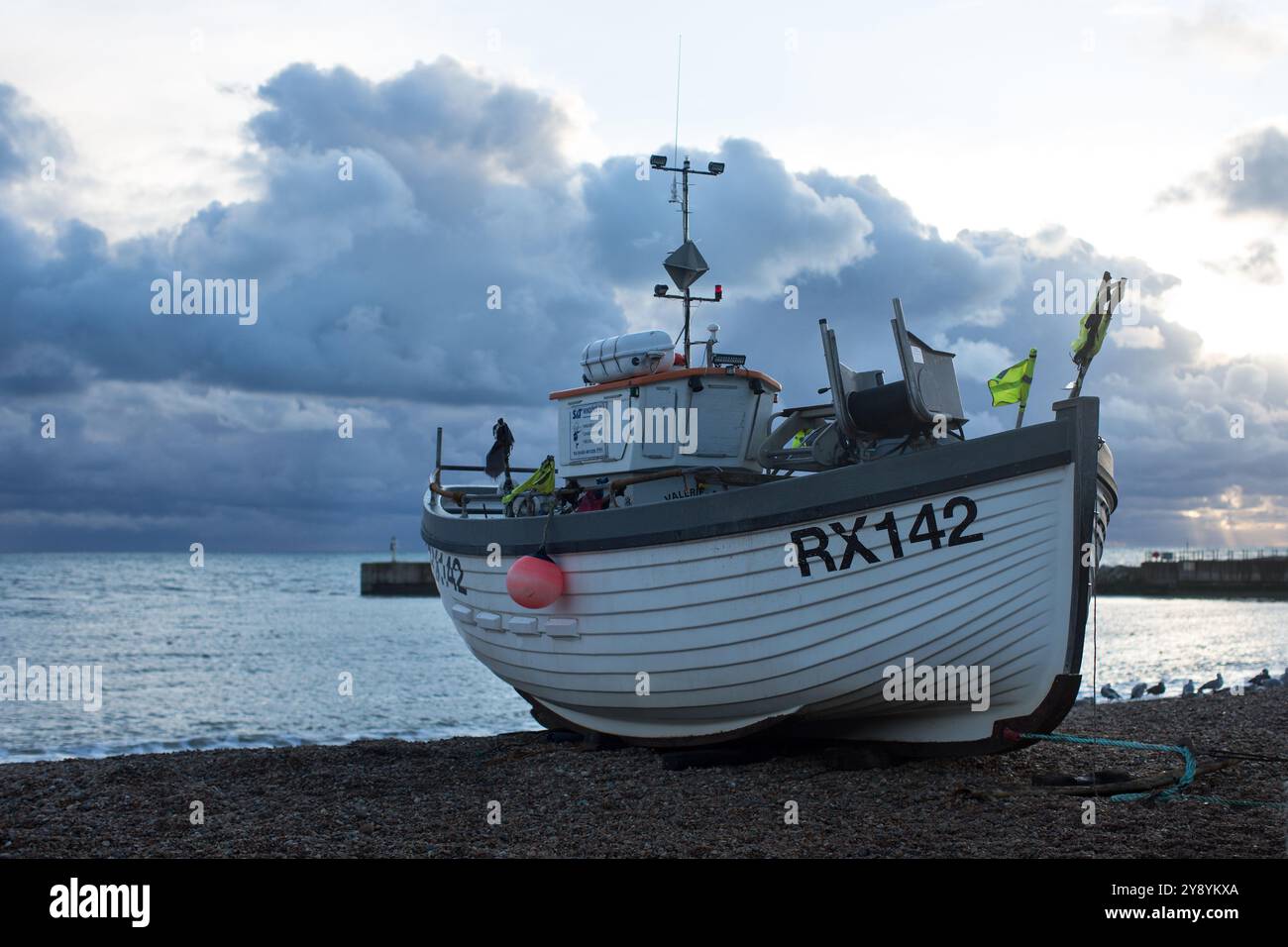 Ein traditionelles Fischerboot ruht an der Kieselküste in Hastings, während sich stürmische Wolken über dem ruhigen Meer sammeln. Stockfoto