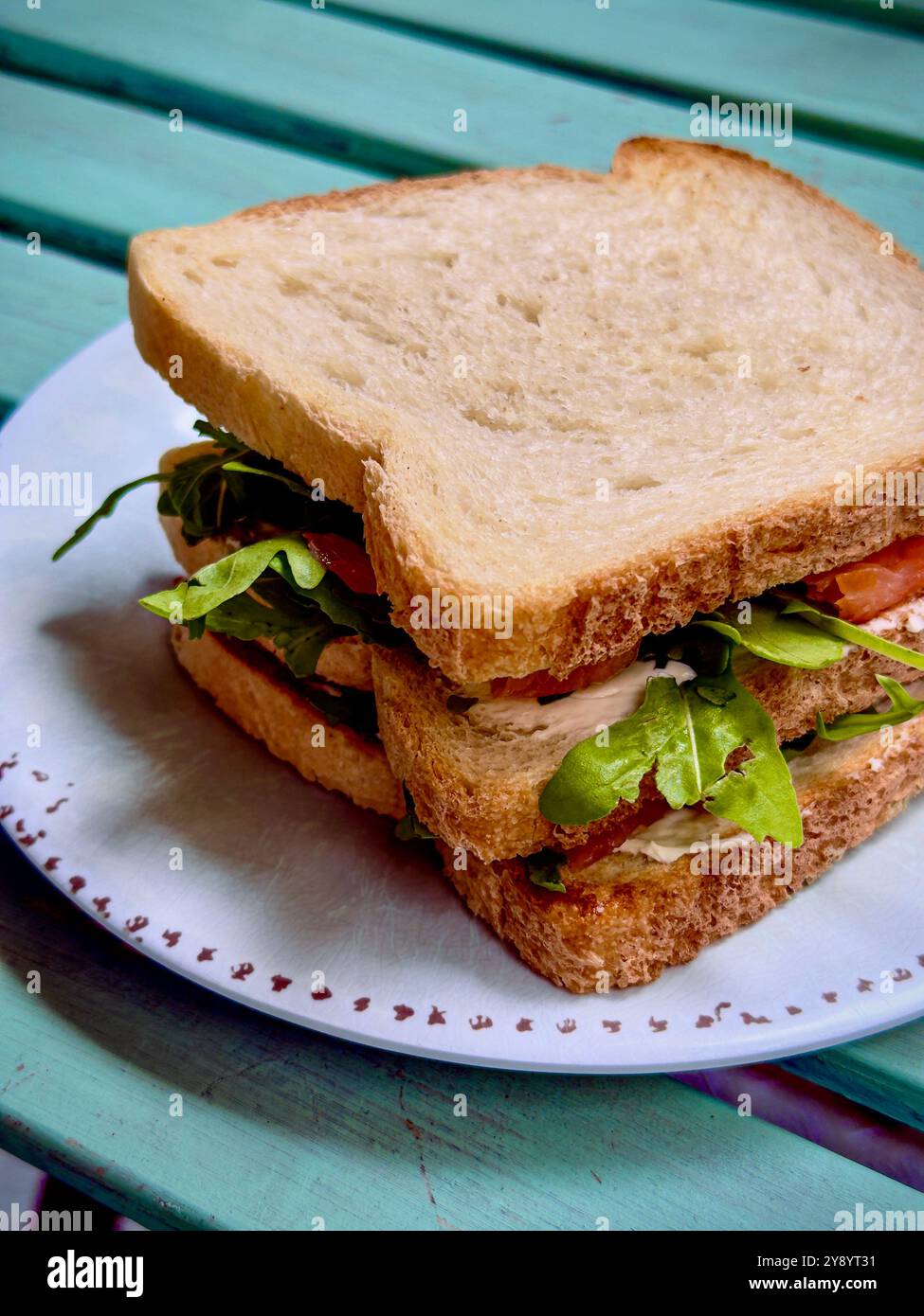 Nahaufnahme eines frischen Gemüse-Sandwiches mit weißem Brot, gefüllt mit knusprigem Salat, Tomaten und anderem Gemüse. Serviert auf einem weißen Teller oben Stockfoto