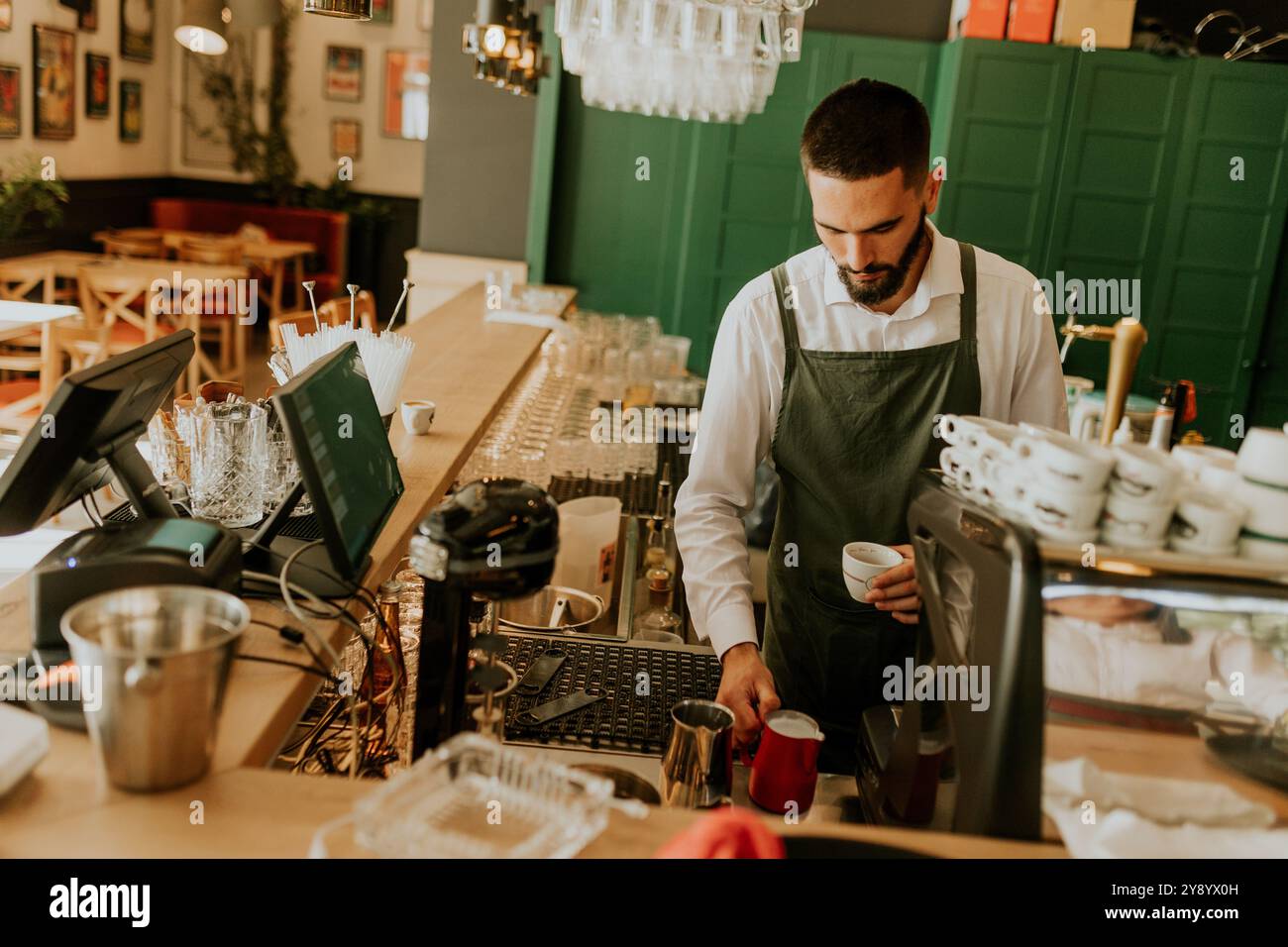 In einem warmen und einladenden Café gießt ein engagierter Barista fachmännisch Milch in eine Kaffeetasse und sorgt so für ein angenehmes Erlebnis für Gäste. Stockfoto