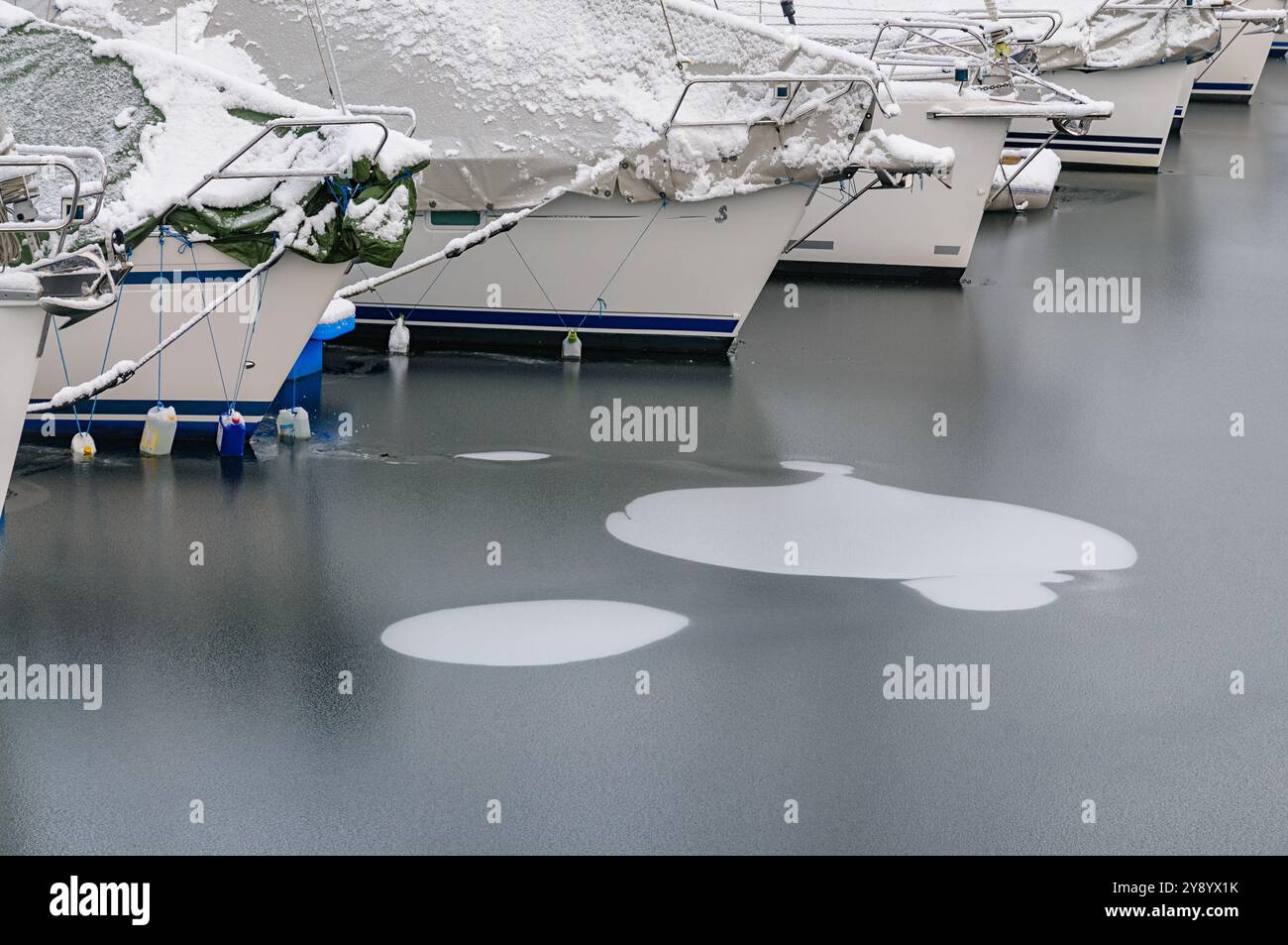 Boote liegen ruhig in einem verschneiten Hafen, umgeben von einer gefrorenen Landschaft, die im sanften Morgenlicht glitzert. Stockfoto