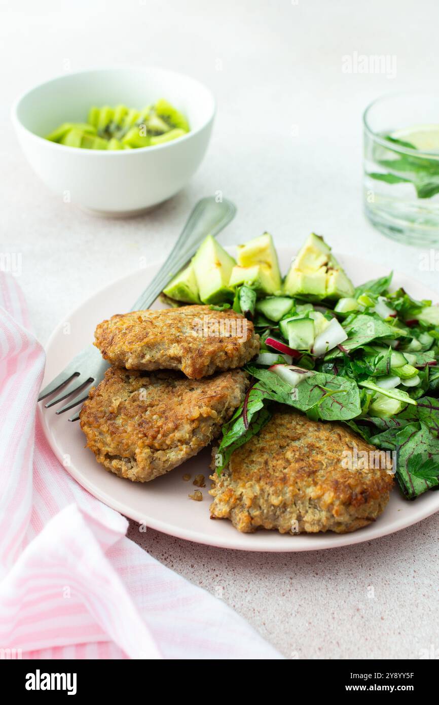 Quinoa-Schnitzel und gemischter Salat mit Avocado und Radieschen, Kiwi und Wasser mit Zitrone, köstliches herzhaftes Frühstück, veganer Lunch-Teller Stockfoto