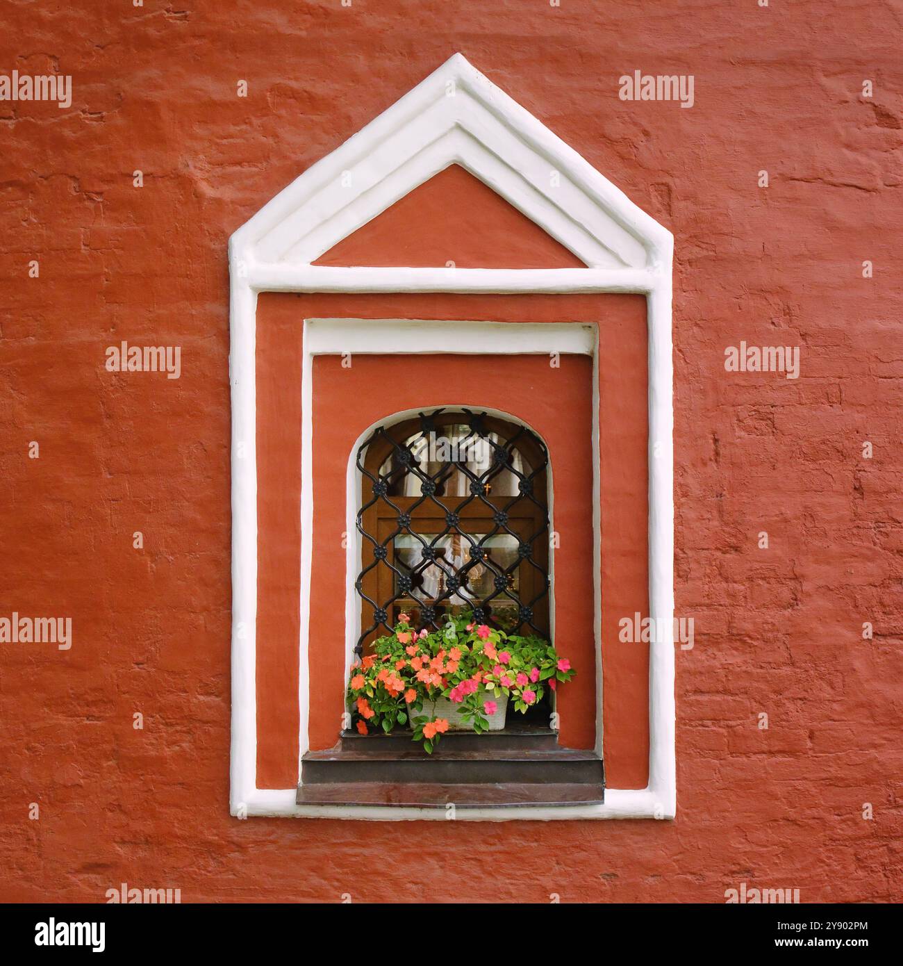 Ein altes weißes Fenster mit Blumen an einer roten Wand. Fensterschmuck in der Architektur. Stockfoto