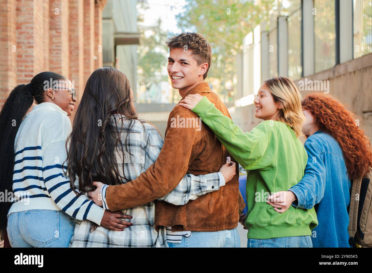 Eine Gruppe von Studenten läuft auf dem Universitätscampus, während einer von ihnen zurückkehrt und lächelnd in die Kamera schaut. Multirassische Teenager-Freunde auf der Highschool gehen in die Klasse, um zusammen zu lernen. Hochwertige Fotos Stockfoto