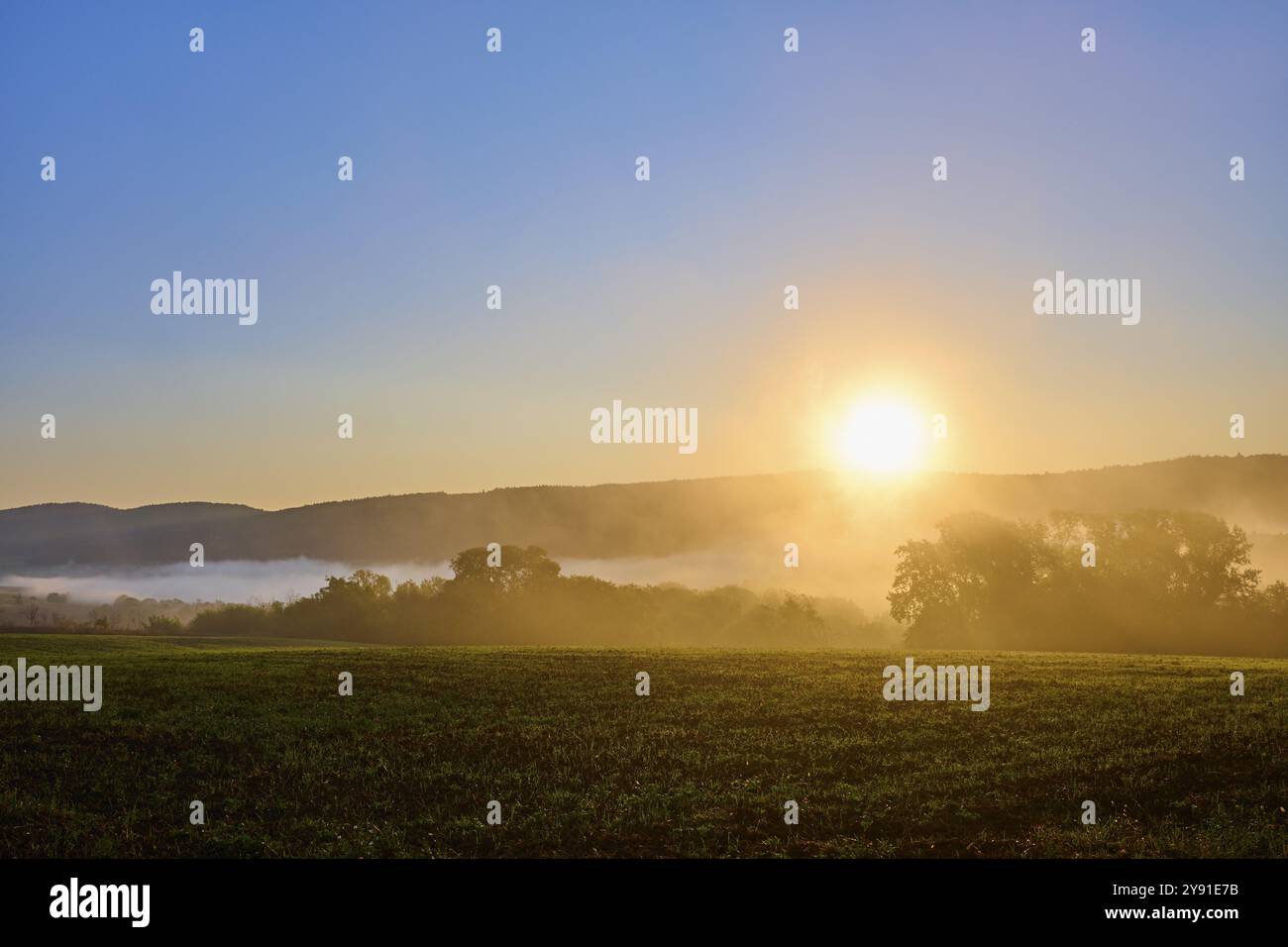Sonnenaufgang über einem nebeligen Maisfeld mit Wald, im Hintergrund Hügel unter klarem Himmel, Grossheubach, Miltenberg, Spessart, Bayern, Deutschland, Europa Stockfoto