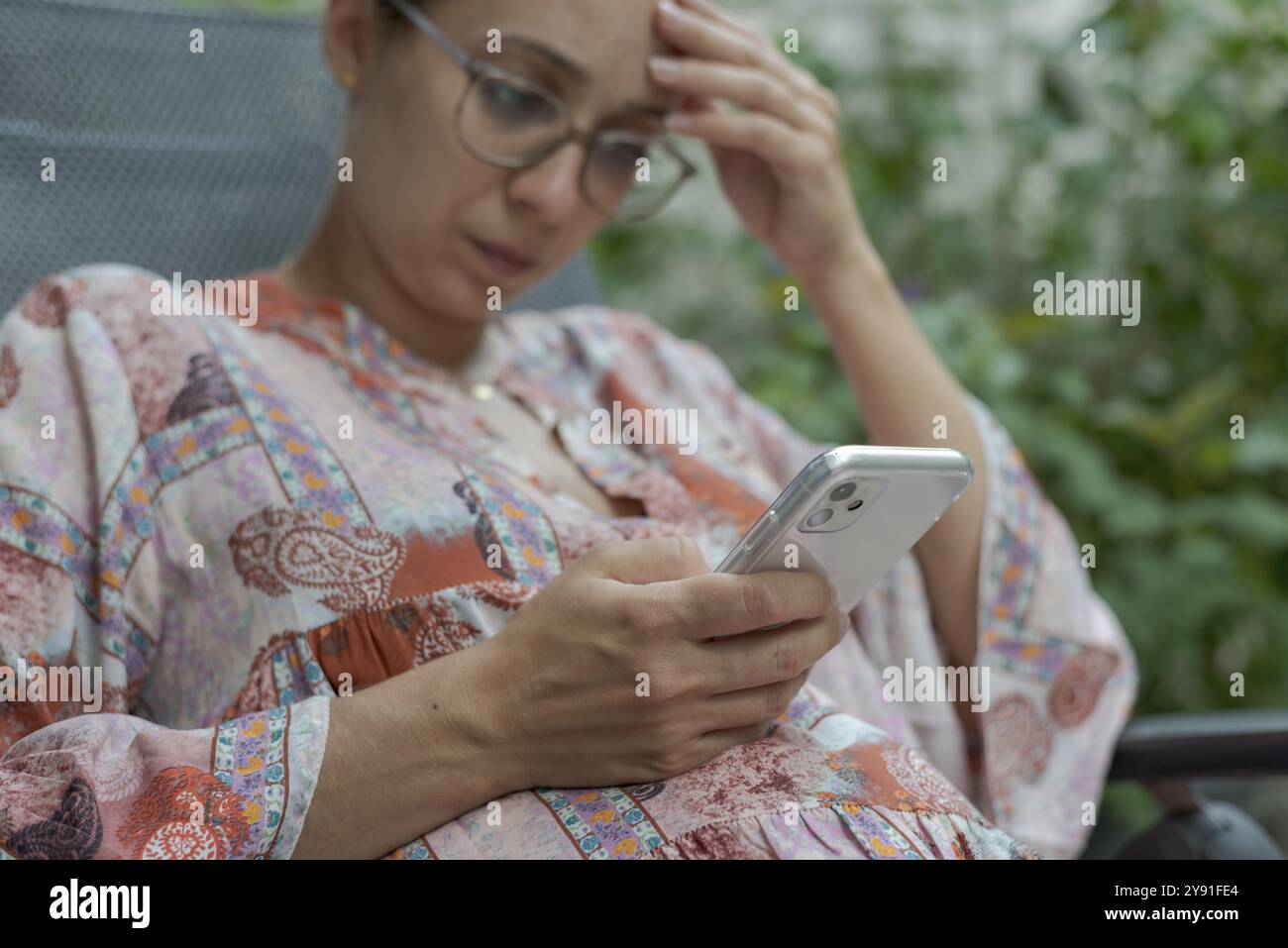 Eine durchdachte Frau mit Brille schaut sich in einer entspannten Umgebung ein Smartphone an Stockfoto