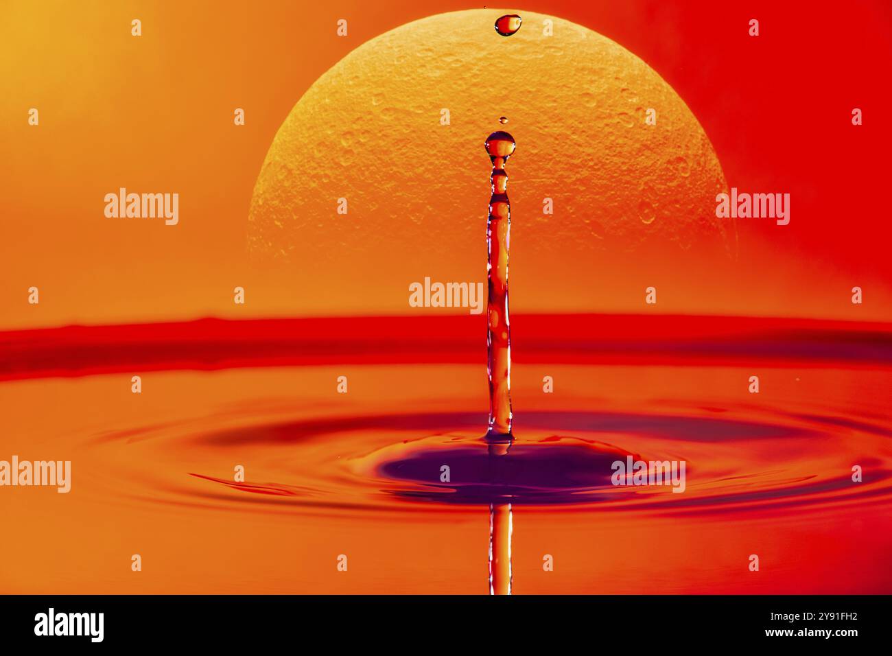 Ein einziger Tropfen Wasser, der in ein Gewässer fällt, mit einem glühenden Sonnenuntergang im Hintergrund, Saturn, Fotomontage, Hochgeschwindigkeitsfotografie Stockfoto