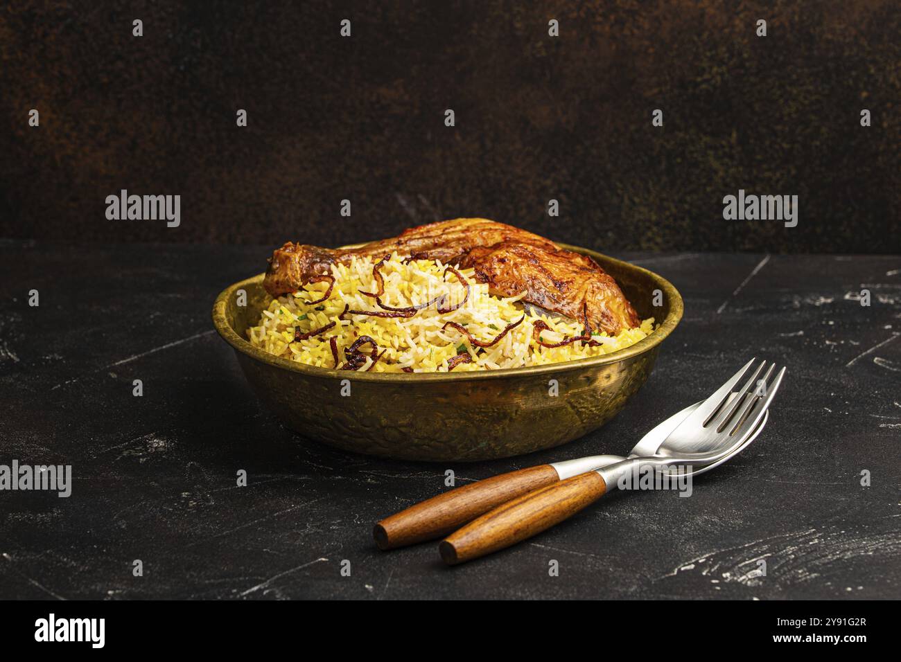 Köstliches indisches Gericht, Biryani Hähnchenschenkel mit Basmati-Reis in einer alten Metallschale aus Messing auf einem Tisch, dunkler rustikaler Hintergrund. Traditionelle nicht-vegetarische Speisen o Stockfoto