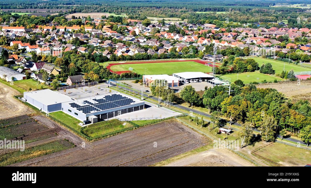Luftaufnahme eines modernen Lagerhauses mit Solarpaneelen in der ländlichen deutschen Stadt, die die Nutzung erneuerbarer Energien und den Kontrast zur natürlichen Landschaft zeigt Stockfoto