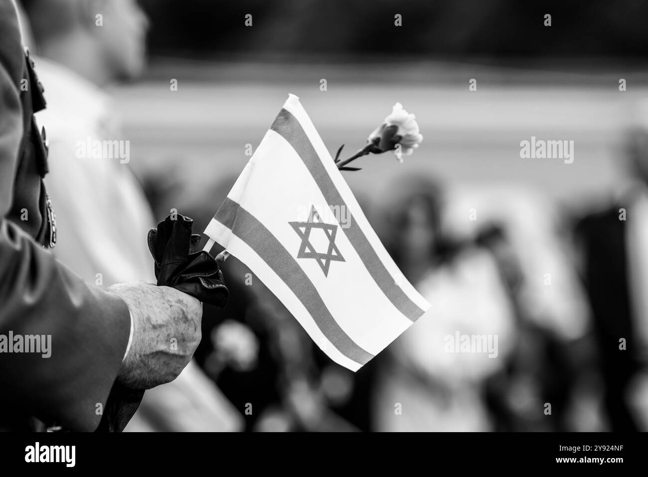 Details with the hands of a man holding the Israeli flag and a flower during a ceremony commemorating the October 2023 attacks. Stockfoto