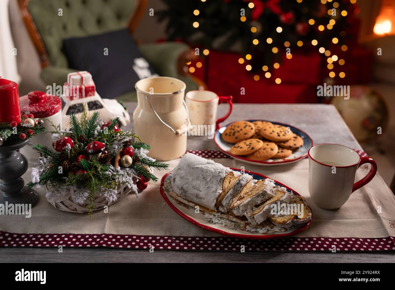 Weihnachtstisch mit Stollenkuchen, Tassen, Keksen auf dem Hintergrund von dekoriertem Weihnachtsbaum und Kamin, gemütliche Weihnachtsatmosphäre Stockfoto