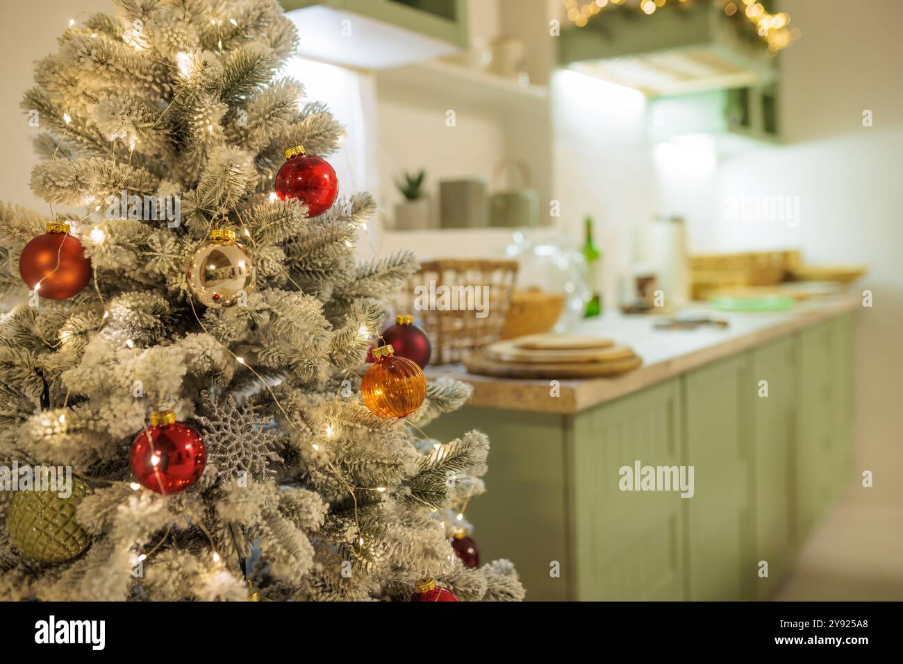 Wunderschön dekorierter Weihnachtsbaum mit roten und goldenen Ornamenten, beleuchtet von warmweißen Lichtern. Im Hintergrund befindet sich eine gemütliche Küche mit festlichem d Stockfoto
