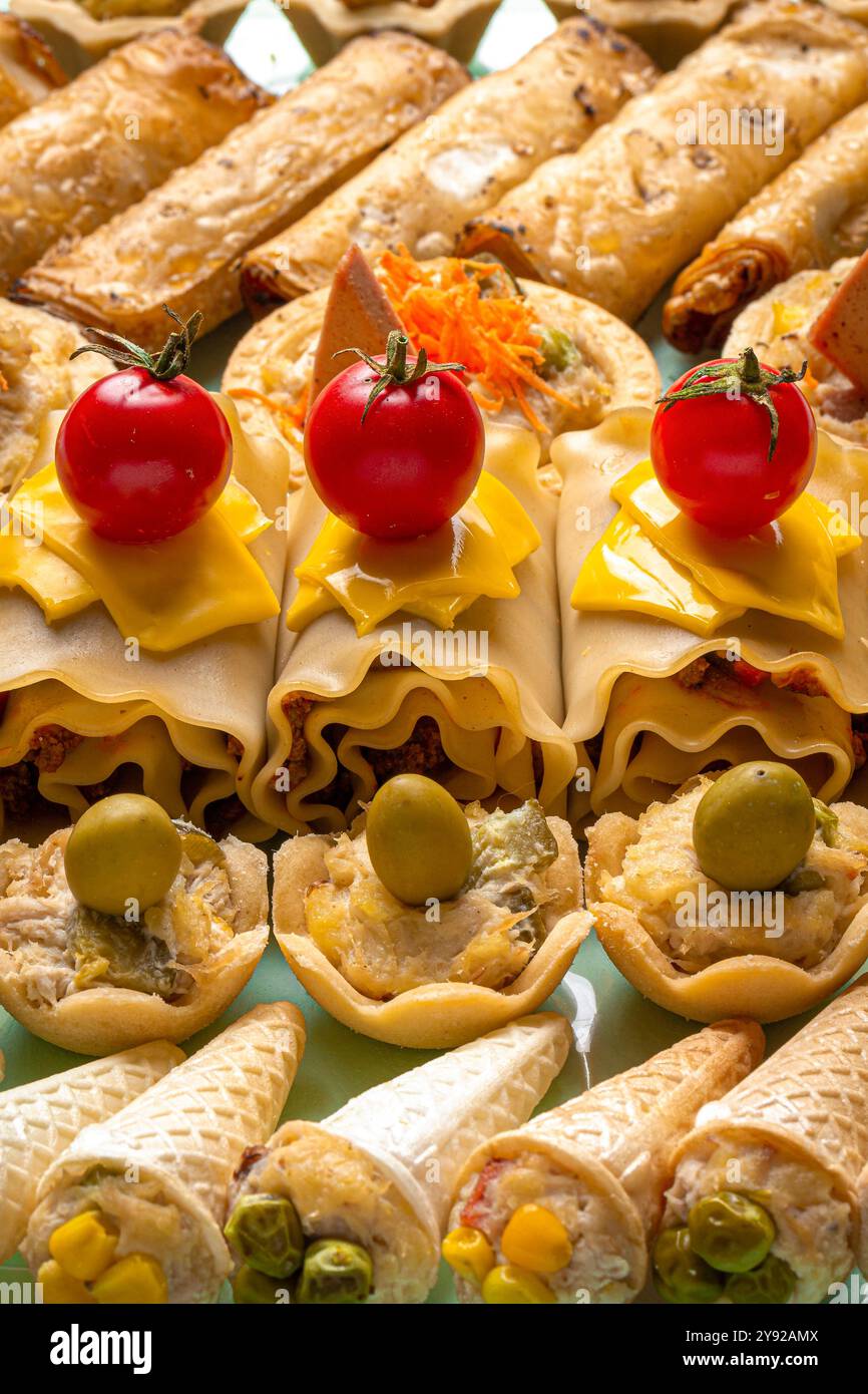 Eine lebhafte Nahaufnahme mit verschiedenen herzhaften Snacks, darunter Lasagna-Brötchen mit Kirschtomaten, Mini-Torten mit Oliven und kegelförmige Vorspeisen. Stockfoto