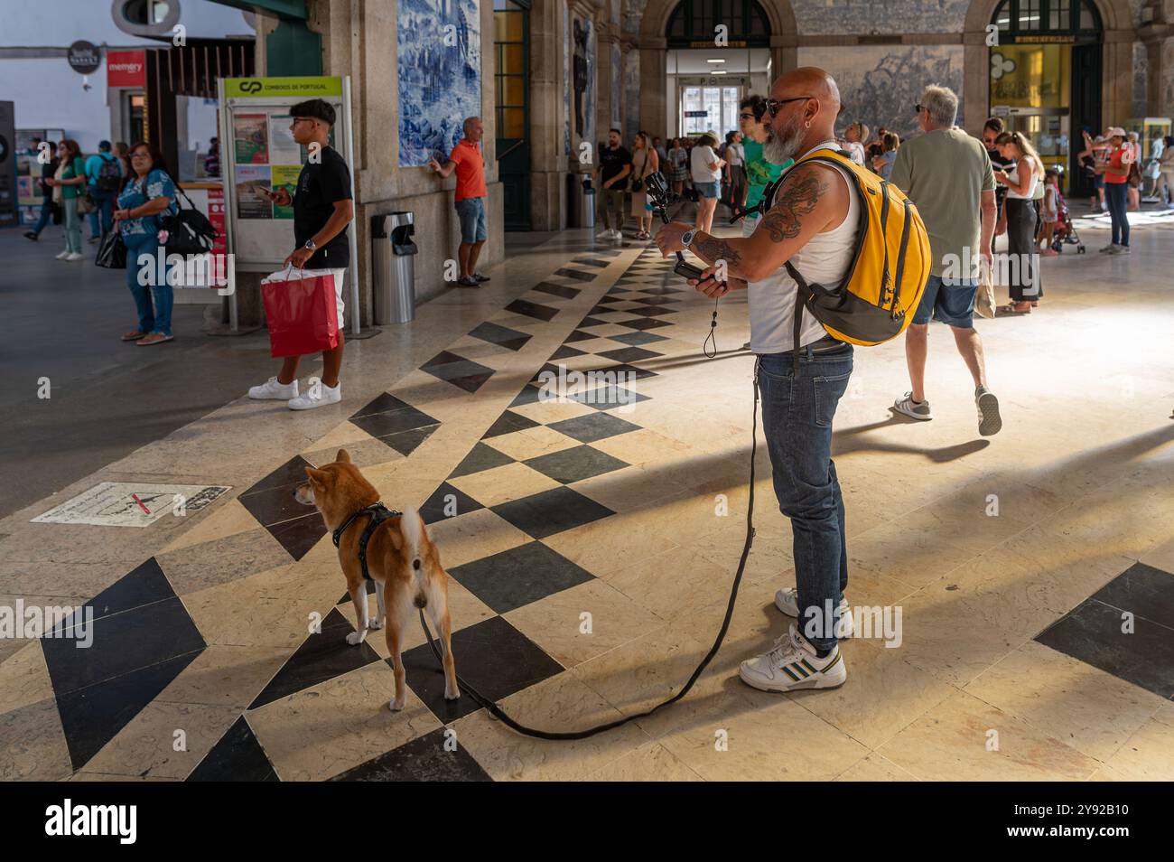 Porto, Portugal - 12. September 2024 : Ein Mann mit Rucksack geht mit seinem Hund und genießt eine lebhafte Bahnhofsatmosphäre. Stockfoto