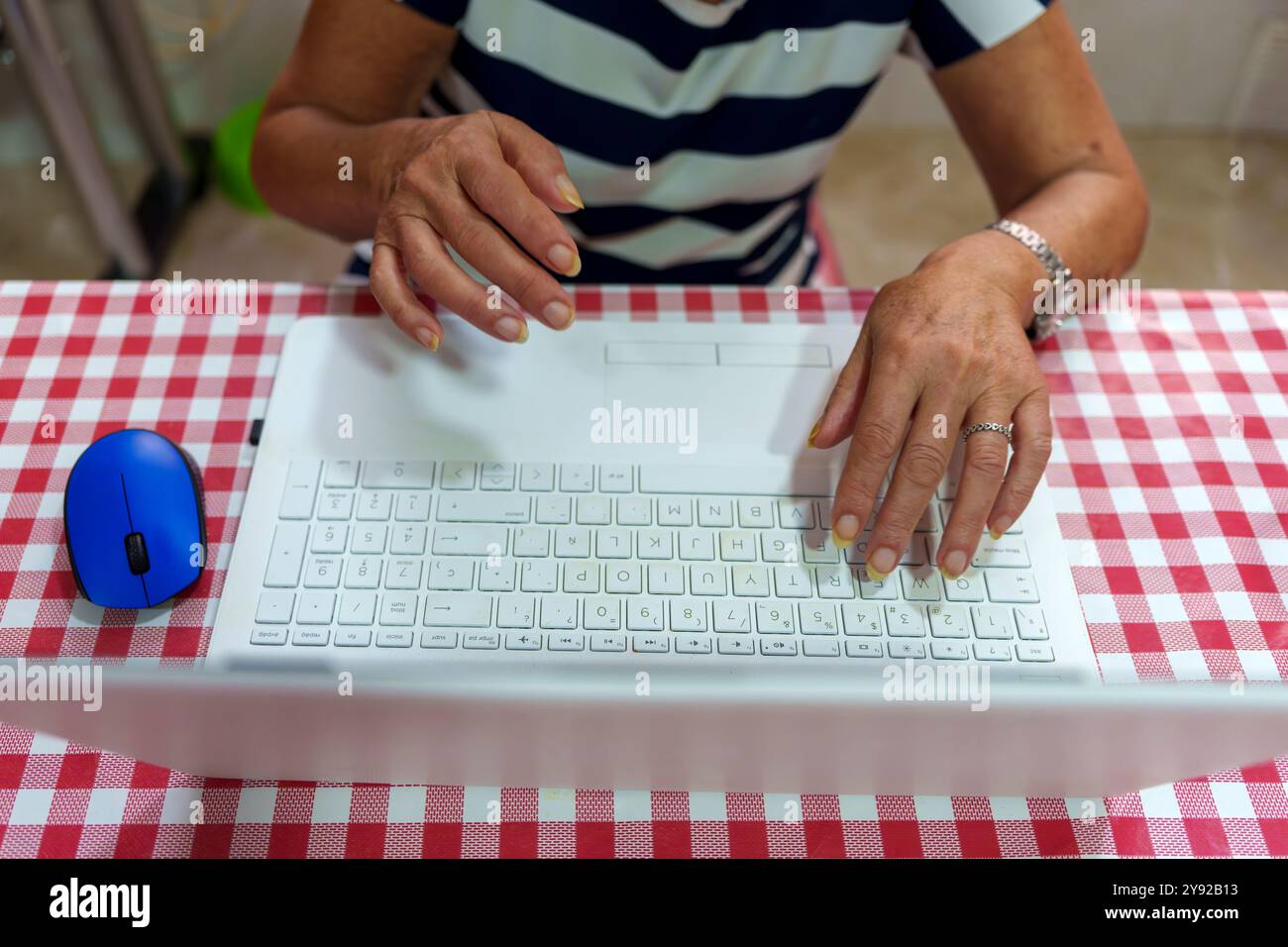 Ältere Hände, die mit der blauen Maus auf der Laptop-Tastatur schreiben: Lerntechnologie zu Hause Stockfoto
