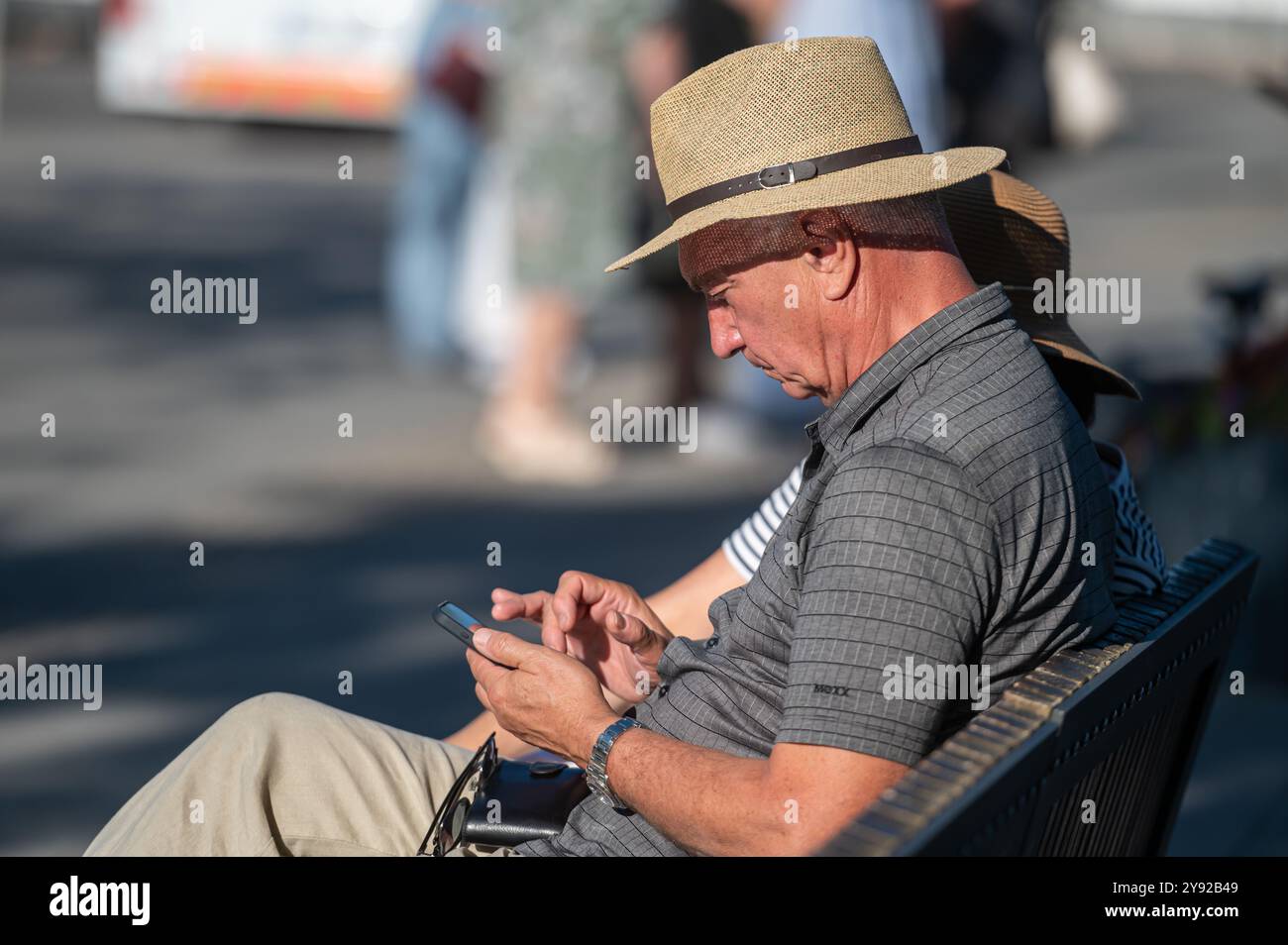 Porto, Portugal - 10. September 2024 : Ein Mann mit Strohhut konzentriert sich auf sein Smartphone, während er draußen sitzt. Stockfoto