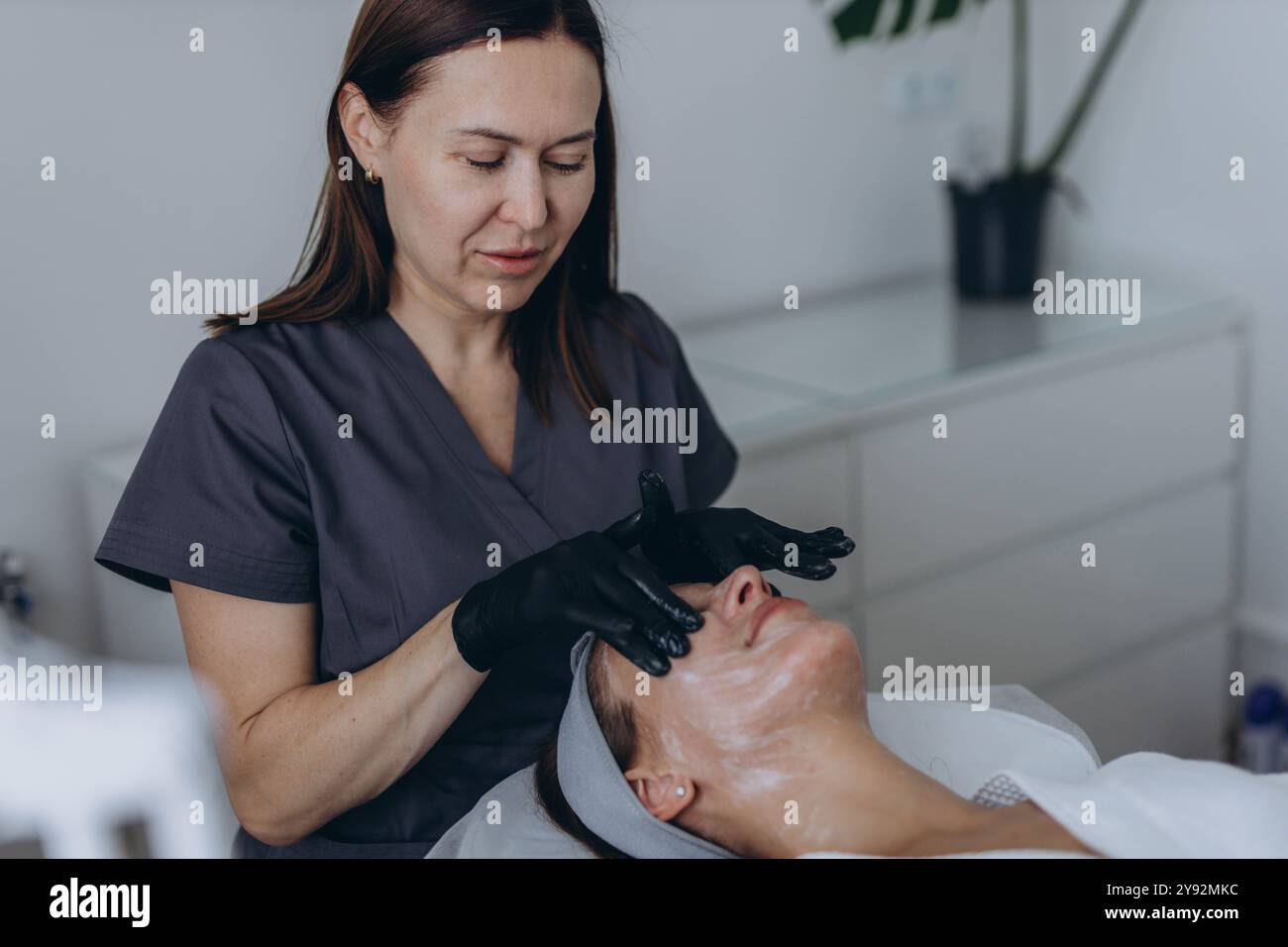 Die Kosmetikerin führt eine Gesichtspeeloperation an einer jungen Frau durch. Hochwertige Fotos Stockfoto