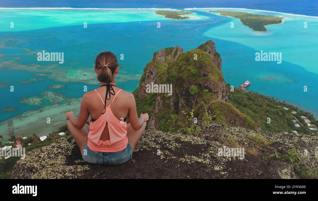 Die junge Frau übt Yoga und genießt einen Moment der Ruhe, während sie die malerische Aussicht auf die Lagune der Insel maupiti in französisch-polynesien bewundert Stockfoto