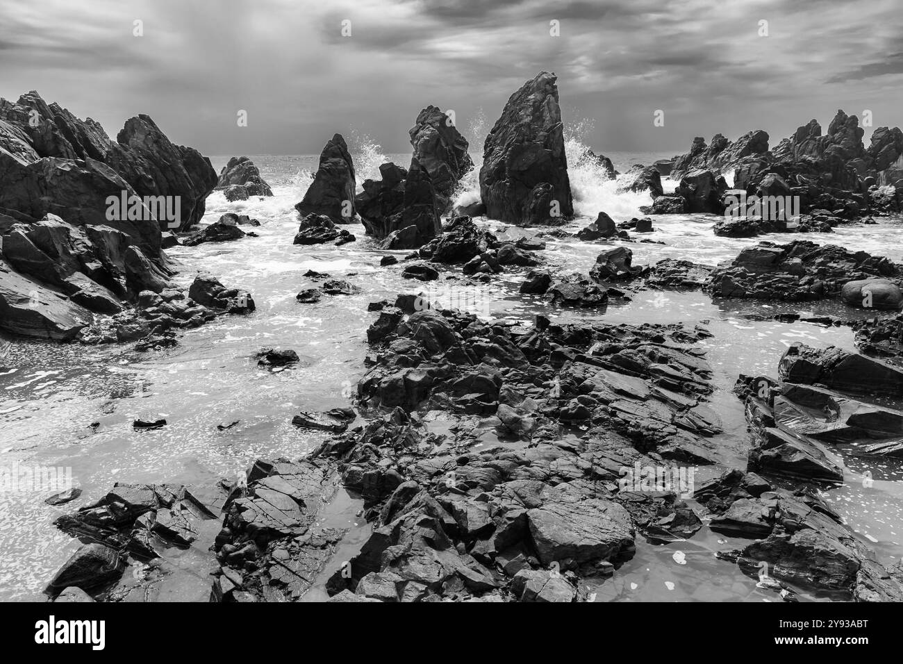 Felsiger Strand an einem sonnigen Tag mit sauberem Wiesenhimmel Panorama. Natürliche Gesteinsbildung. Querformat in Schwarzweiß. Stockfoto