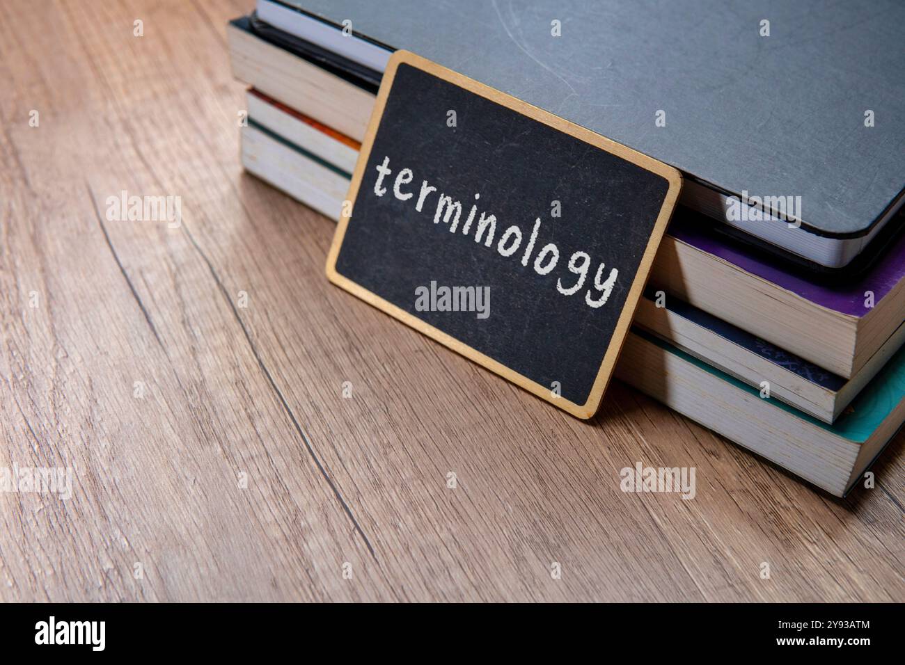 Eine Tafel mit dem Wort „TERMINOLOGIE“ wird auf einen Stapel Lehrbücher auf einem Holztisch gelegt. Kopierbereich für Text. Stockfoto