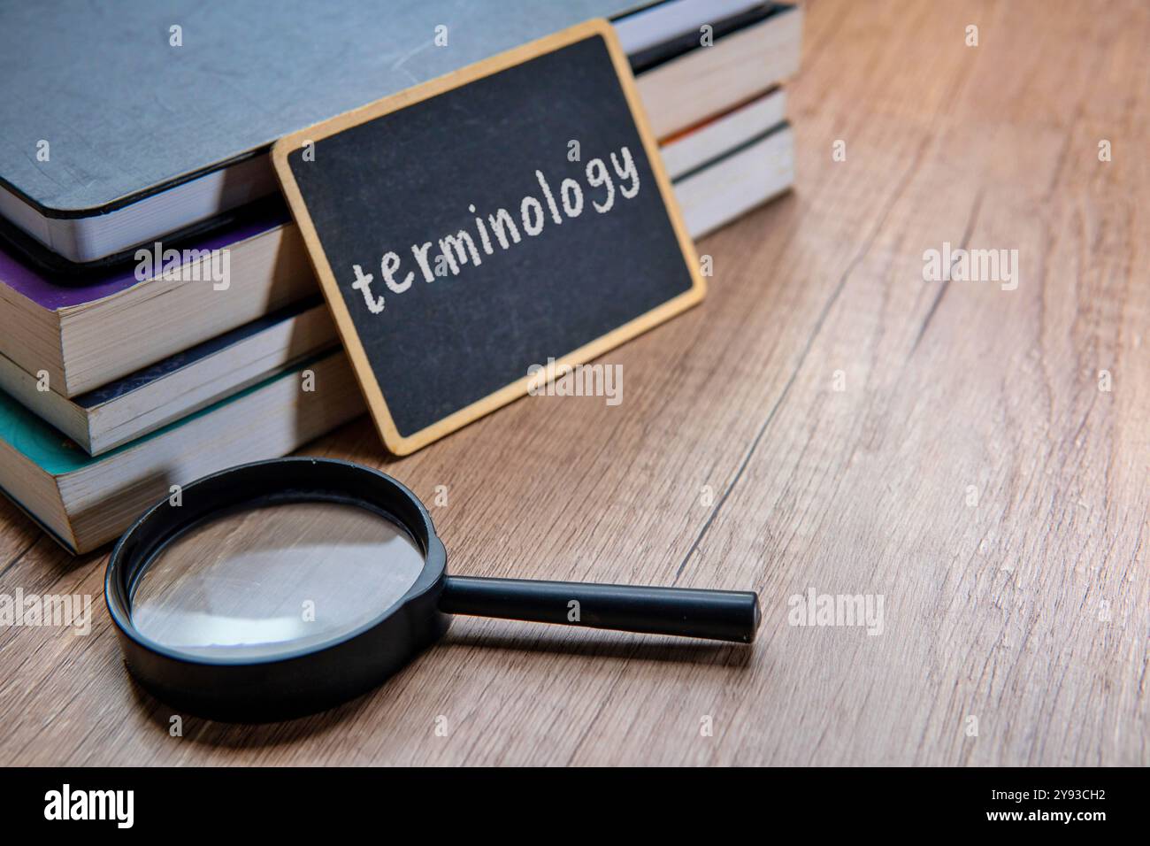 Eine Tafel mit dem Wort „TERMINOLOGIE“ wird auf einen Stapel Lehrbücher auf einem Holztisch gelegt. Kopierbereich für Text. Stockfoto