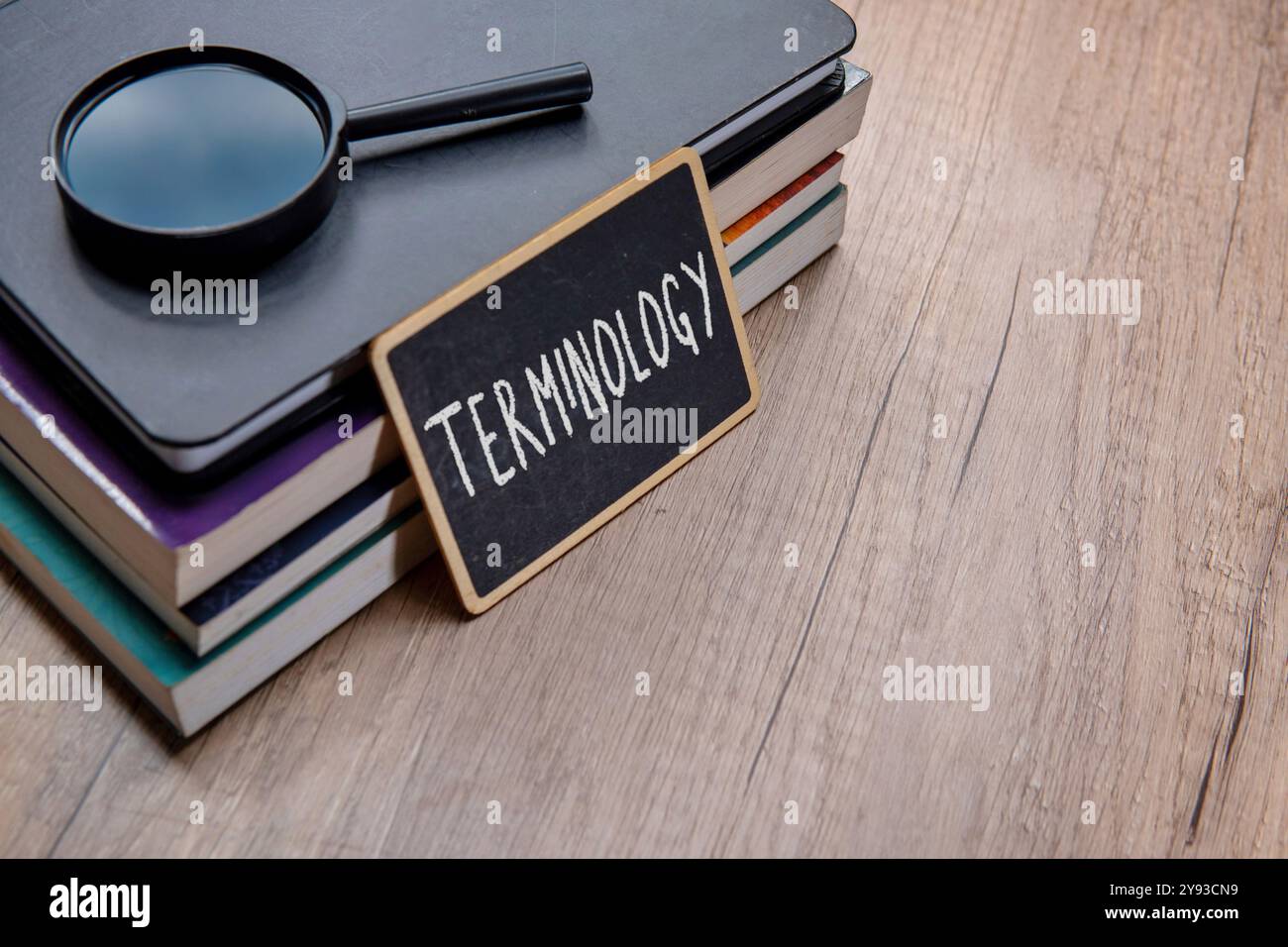 Eine Tafel mit dem Wort „TERMINOLOGIE“ wird auf einen Stapel Lehrbücher auf einem Holztisch gelegt. Kopierbereich für Text. Stockfoto