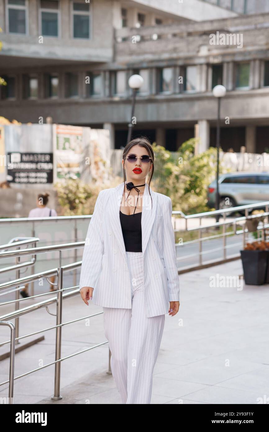 Stilvolle junge Frau in gestreiftem Anzug, die selbstbewusst auf der City Street unterwegs ist. Stockfoto
