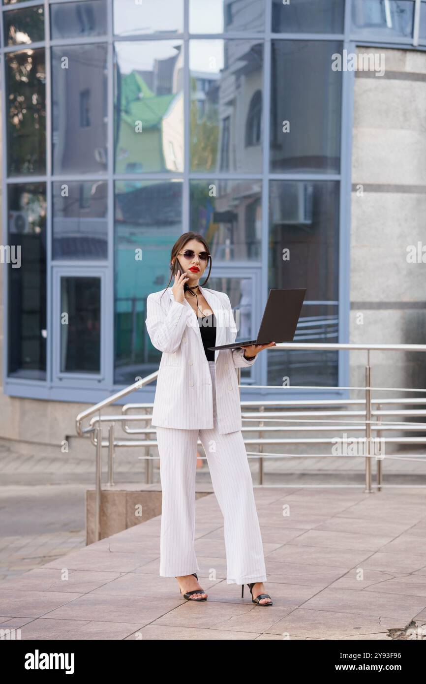 Stilvolle Geschäftsfrau mit Laptop in urbanem Ambiente. Stockfoto