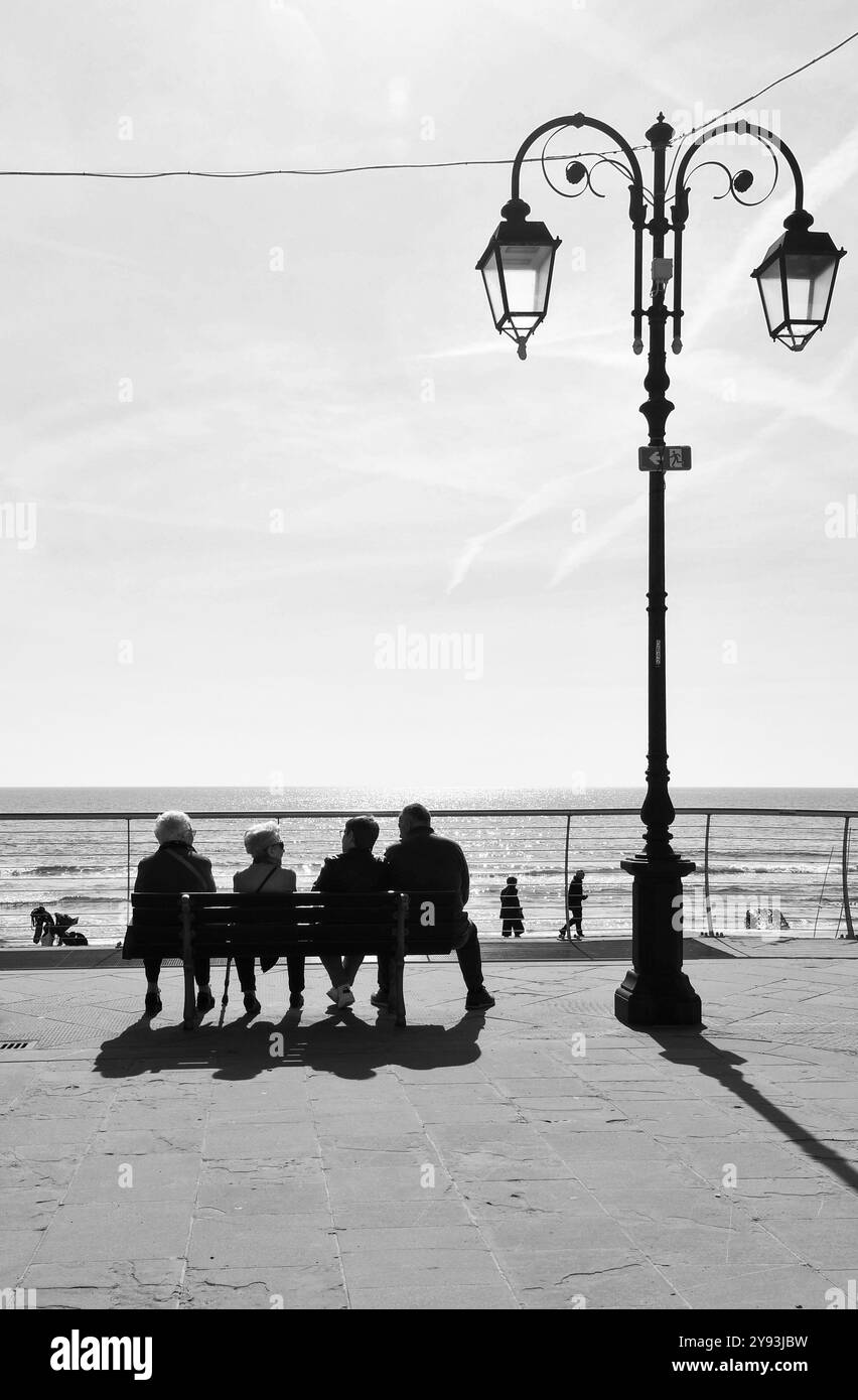 Schwarzweißfoto. Drei ältere Damen und ein Gentleman ruhen auf einer Bank an der Promenade des Ferienorts Alassio, Savona, Ligurien, Italien Stockfoto